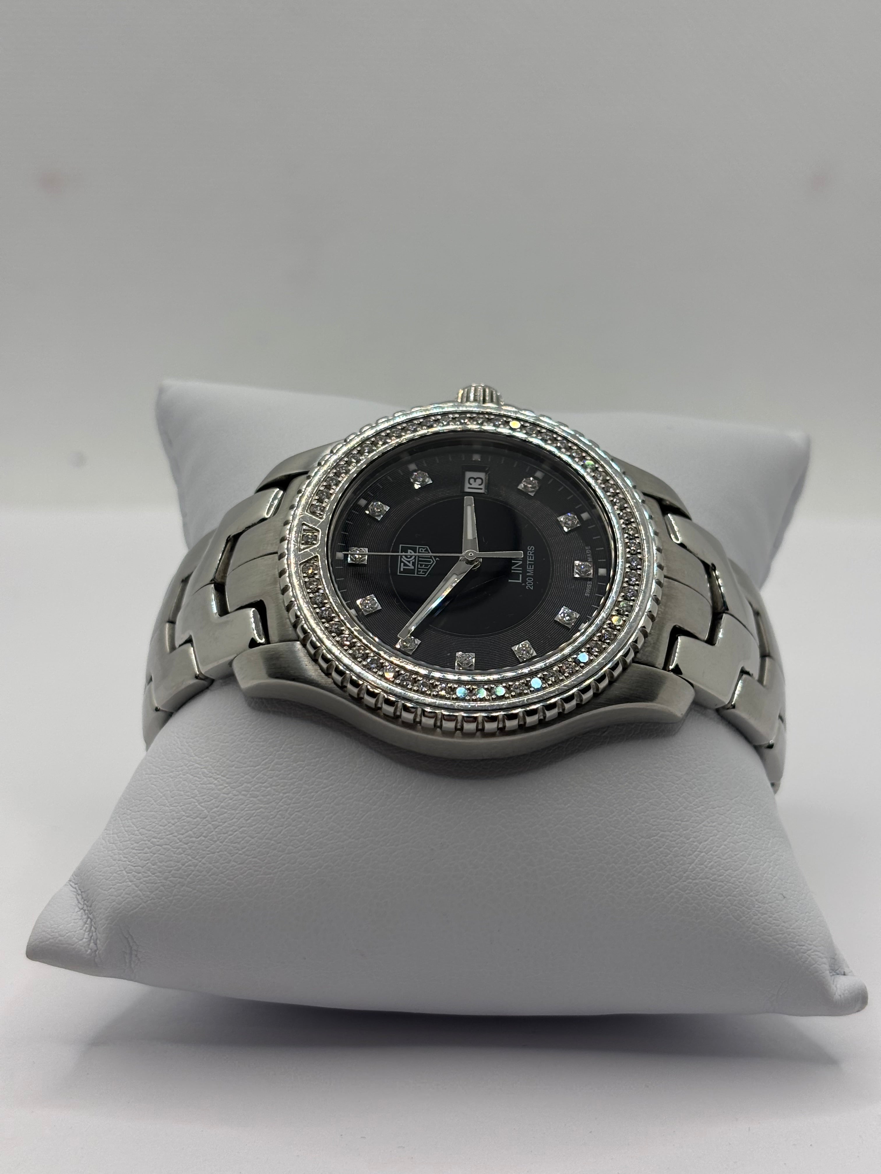 Luxury Tag Heuer wristwatch with black dial and diamond accents displayed on a white cushion, watches collection